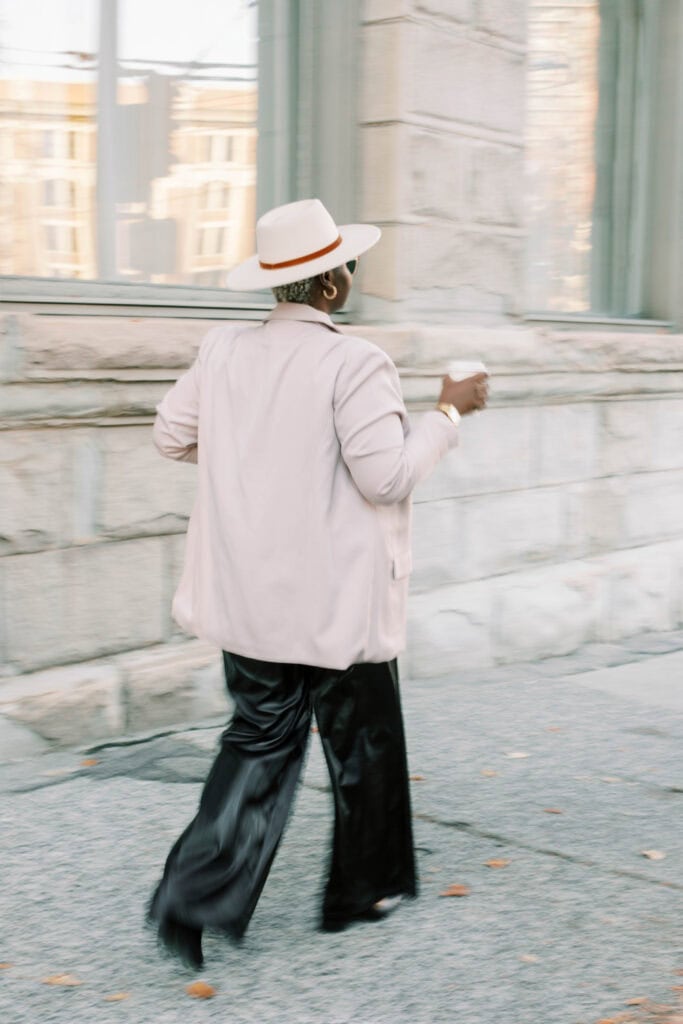 Stylish plus-size woman walking confidently in black leather pants and a white blazer, representing body-positive dress brands and inclusive fashion.