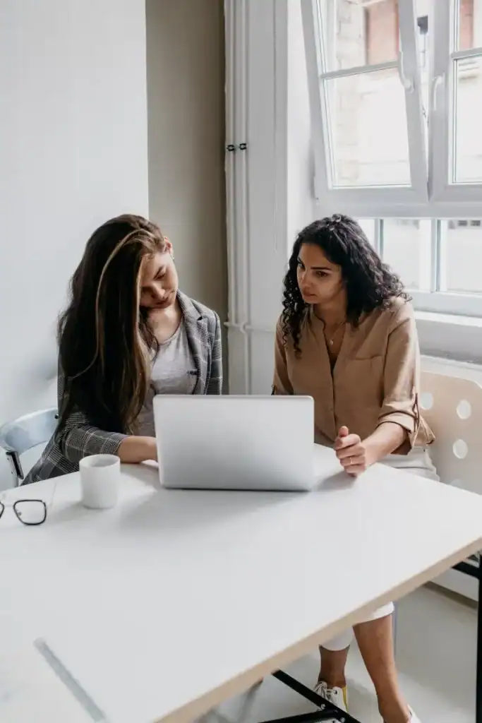 Two professional women talking at a desk with a laptop, discussing work styles and right-brained strengths.